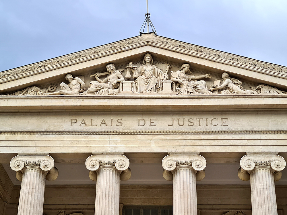 Façade du Palais de Justice avec des sculptures représentant la justice et la loi, colonnes classiques et ciel nuageux.